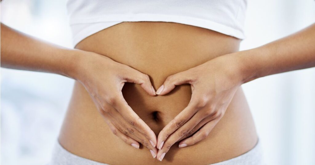 Woman forming a heart shape with her hands over her lower abdomen, symbolizing gut health, self-care, and the mind-body connection.