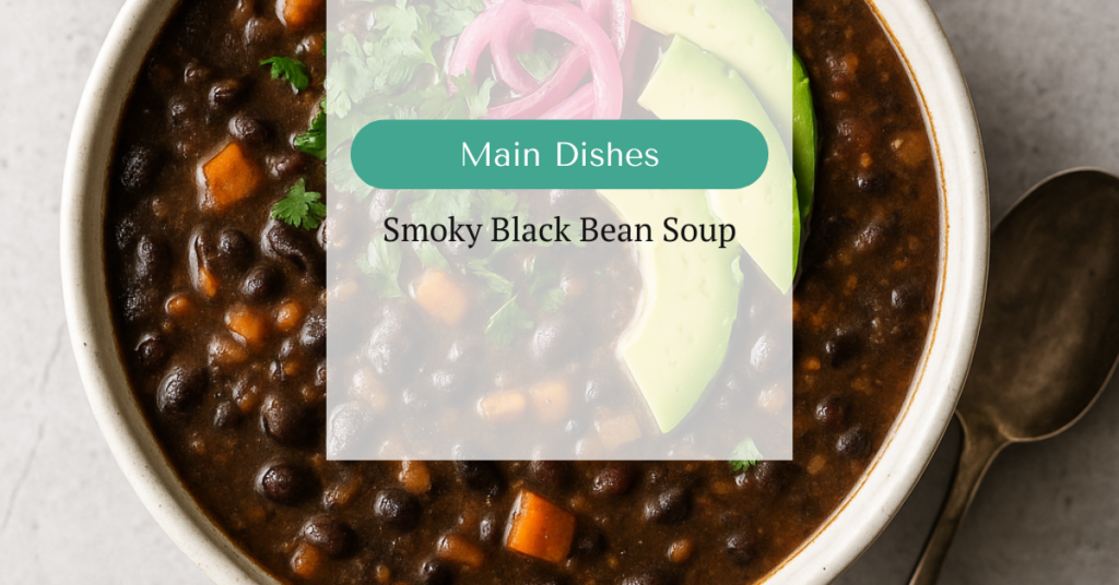Bowl of creamy black bean soup topped with fresh cilantro, avocado slices, and pickled red onions, with a spoon resting beside the bowl.