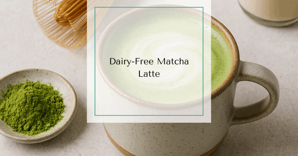 A frothy green matcha latte in a ceramic mug, topped with a light foam swirl, surrounded by matcha powder, a bamboo whisk, and almond milk.