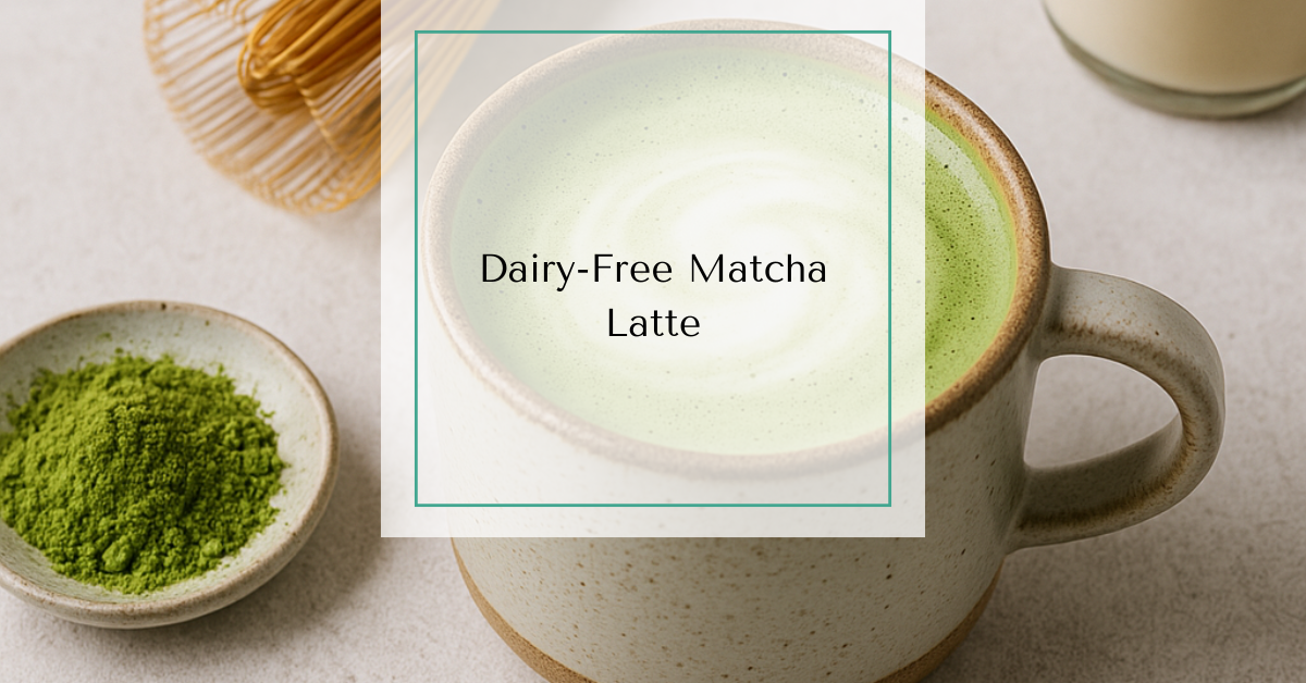 A frothy green matcha latte in a ceramic mug, topped with a light foam swirl, surrounded by matcha powder, a bamboo whisk, and almond milk.