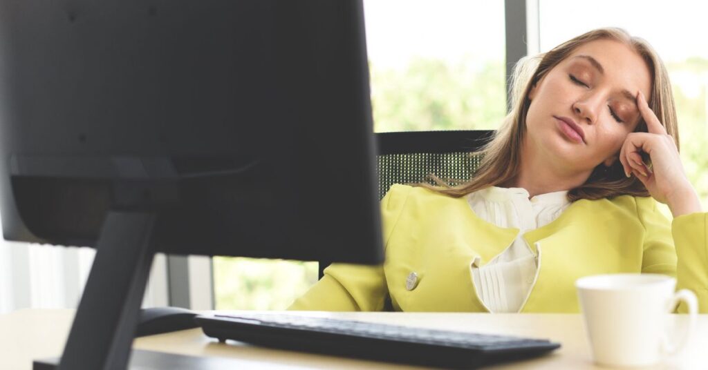 Woman experiencing afternoon slump causes at 3pm with low energy and brain fog while working at a computer