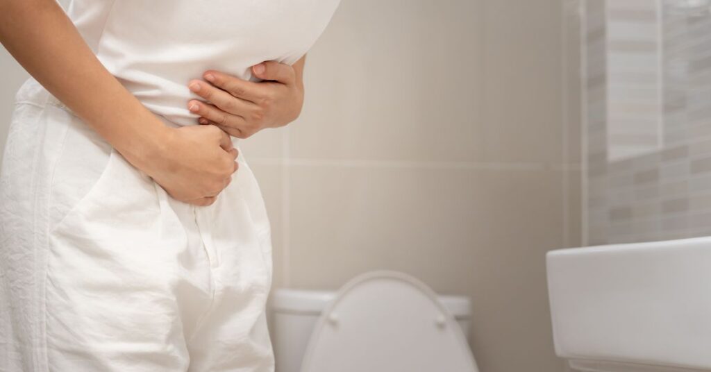 Woman standing in a bathroom holding her stomach.