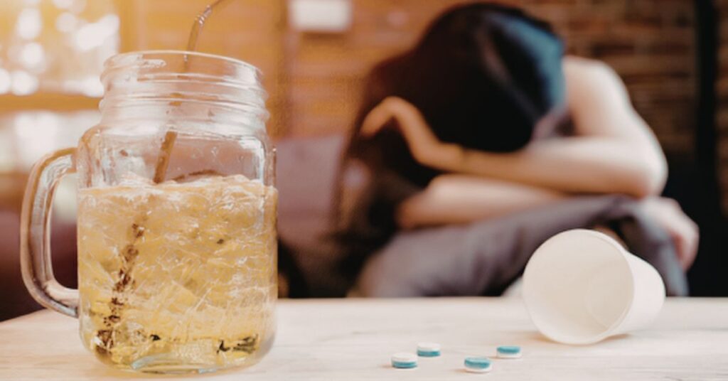 Glass of iced drink, scattered pills, and a woman resting in the background.