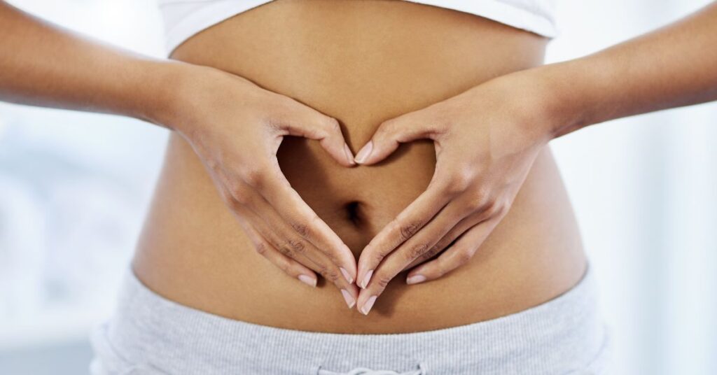 Woman holding her hands in a heart shape over her abdomen.