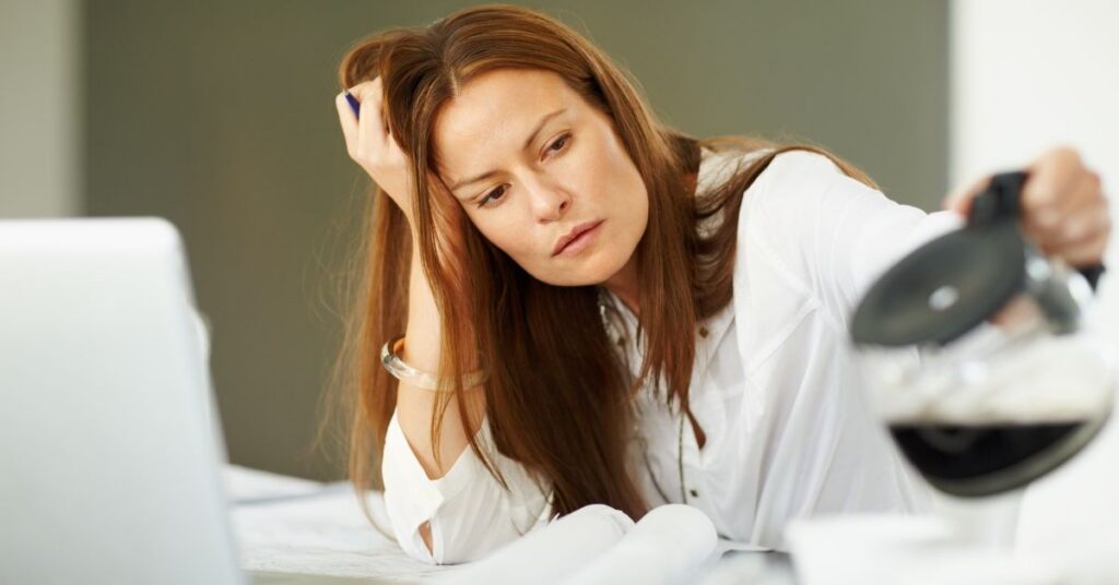 Tired woman at her desk pouring a carafe of coffee.