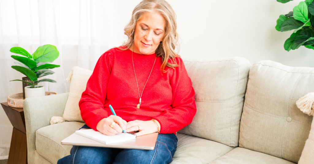 Woman sitting on a couch writing in a notebook.