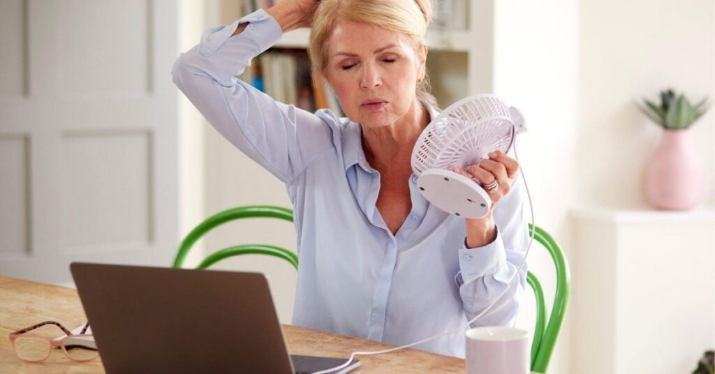 Midlife woman fanning herself during a hot flash for an article about perimenopause symptoms